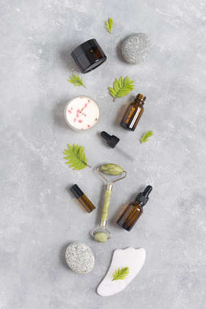 Containers of lotion, essential oils, massage rollers and gouache scraper on a gray concrete background. Natural SPA cosmetic products background. Layout of the beauty salon branding. Flat layの写真素材