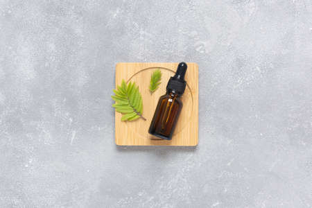 A glass bottle with a pipette for oil, lotion or serum on a wooden stand on a gray concrete background. Layout of the beauty salon brandingの写真素材