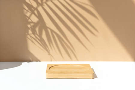 Minimal abstract background for the presentation of a cosmetic product. Wooden scene on a white table. Premium podium with a shadow of tropical palm leaves on a beige wall. Showcase, display case.の写真素材