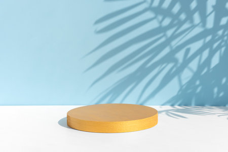 Minimal abstract background for the presentation of a cosmetic product. A cylindrical golden scene on a white table. Premium podium with a shadow of tropical palm leaves on a blue wall. Showcaseの写真素材
