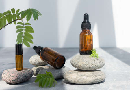 Bottles of dark amber glass of lotion or essential oil on gray stones. Natural SPA cosmetic products background. Layout of the beauty salon brandingの写真素材
