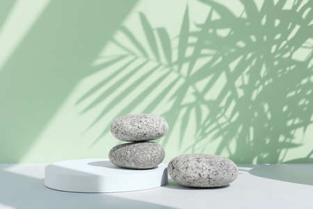 A podium made of stones on a gray table against a green wall with a shadow from the leaves of a palm tree. Showcase for product promotion, beauty, natural cosmeticの写真素材