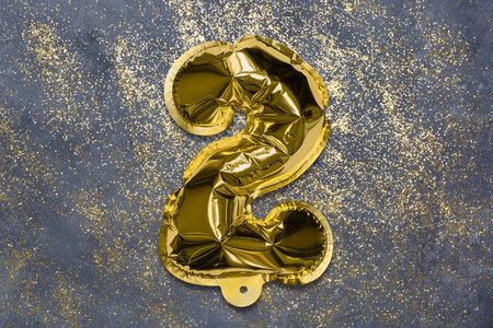 The number of the balloon made of golden foil, the number two on a gray background with sequins. Birthday greeting card with inscription 2. Top view. Numerical digit, Celebration event, template.の写真素材