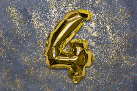 The number of the balloon made of golden foil, the number four on a gray background with sequins. Birthday greeting card with inscription 4. Top view. Numerical digit, Celebration event, template.の写真素材
