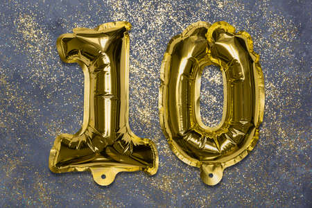 The number of the balloon made of golden foil, the number ten on a gray background with sequins. Birthday greeting card with inscription 10. Anniversary concept. Numerical digit, Celebration event.の写真素材