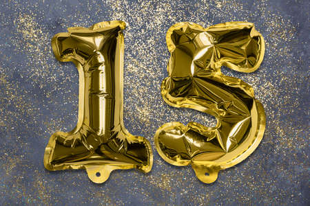 The number of the balloon made of golden foil, the number fifteen on a gray background with sequins. Birthday greeting card with inscription 15. Anniversary concept. Celebration event.の写真素材