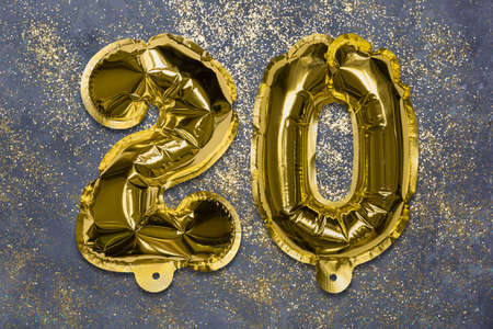 The number of the balloon made of golden foil, the number twenty on a gray background with sequins. Birthday greeting card with inscription 20. Anniversary concept. Numerical digit, Celebration event.の写真素材