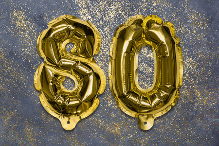 The number of the balloon made of golden foil, the number eighty on a gray background with sequins. Birthday greeting card with inscription 80. Anniversary concept. Celebration event, template.の写真素材