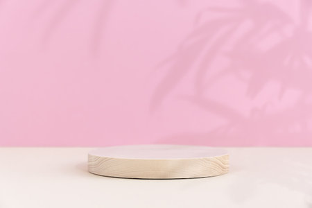 Minimal abstract background for the presentation of a cosmetic product. A cylindrical wooden scene on a beige table. Premium podium with a shadow of tropical palm leaves on a pink wall.の写真素材
