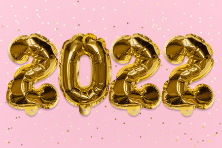Golden foil balloons made numbers 2022 on a pink background with golden sequins. New Years card....
