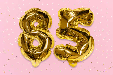 The number of the balloon made of golden foil, the number eighty-five on a pink background with sequins. Birthday greeting card with inscription 85. Anniversary concept. Celebration event.の写真素材