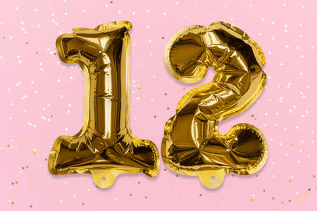 The number of the balloon made of golden foil, the number twelve on a pink background with sequins. Birthday greeting card with inscription 12. Top view. Numerical digit, Celebration event, template.の写真素材
