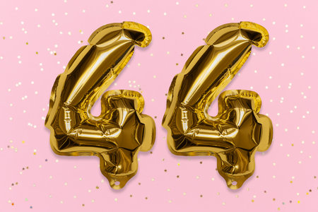 The number of the balloon made of golden foil, the number forty-four on a pink background with...