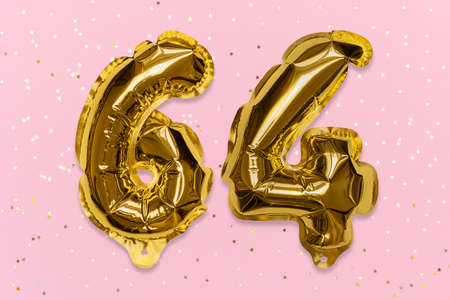 The number of the balloon made of golden foil, the number sixty-four on a pink background with sequins. Birthday greeting card with inscription 64. Numerical digit, Celebration event, template.の写真素材