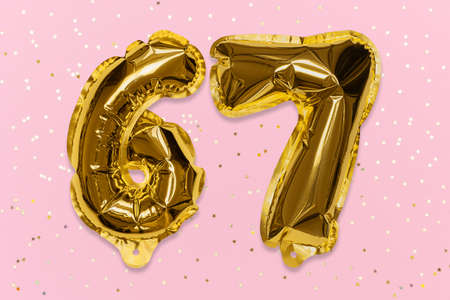 The number of the balloon made of golden foil, the number sixty-seven on a pink background with sequins. Birthday greeting card with inscription 67. Numerical digit, Celebration event, template.の写真素材