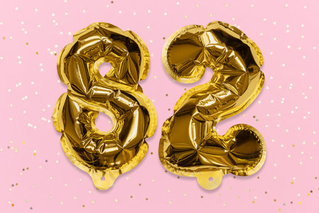 The number of the balloon made of golden foil, the number eighty-two on a pink background with sequins. Birthday greeting card with inscription 82. Numerical digit, Celebration event, template.の写真素材
