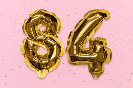 The number of the balloon made of golden foil, the number eighty-four on a pink background with sequins. Birthday greeting card with inscription 84. Numerical digit, Celebration event, template.の写真素材