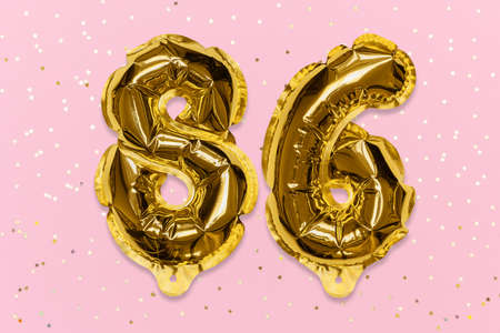 The number of the balloon made of golden foil, the number eighty-six on a pink background with sequins. Birthday greeting card with inscription 86. Numerical digit, Celebration event, template.の写真素材