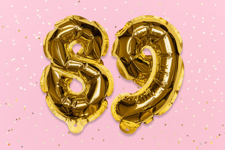 The number of the balloon made of golden foil, the number eighty-nine on a pink background with sequins. Birthday greeting card with inscription 89. Numerical digit, Celebration event, template.の写真素材