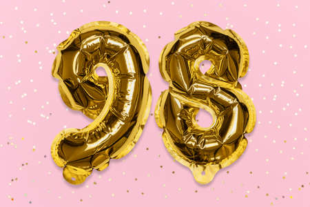 The number of the balloon made of golden foil, the number ninety-eight on a pink background with sequins. Birthday greeting card with inscription 98. Numerical digit, Celebration event, template.の写真素材