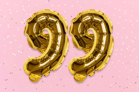 The number of the balloon made of golden foil, the number ninety-nine on a pink background with sequins. Birthday greeting card with inscription 99. Numerical digit, Celebration event, template.の写真素材