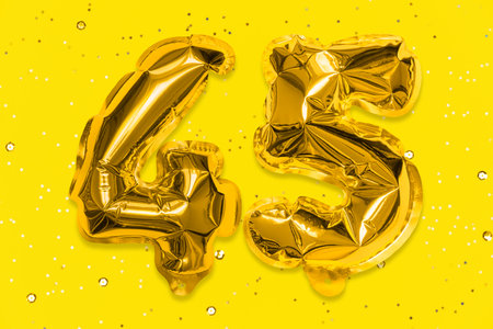 The number of the balloon made of golden foil, the number forty-five on a yellow background with sequins. Birthday greeting card with inscription 45. Anniversary concept. Celebration event.の写真素材
