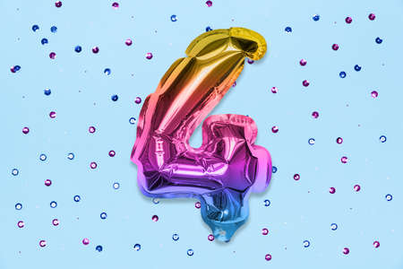 Rainbow foil balloon number, digit four on a blue background with sequins. Birthday greeting card with inscription 4. Top view. Numerical digit. Celebration event, template.の写真素材