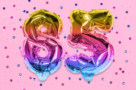 Rainbow foil balloon number, digit eighty five on a pink background with sequins. Birthday greeting card with inscription 85. Anniversary concept. Numerical digit. Celebration event, template.の写真素材