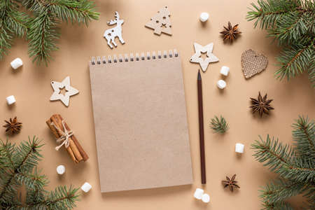 Craftbook, Notepad for wishes. Christmas background with wooden toys, fir branches, cinnamon sticks and marshmallows on a beige table. New year card. Copy space, mock up, flat lay, top view.の写真素材