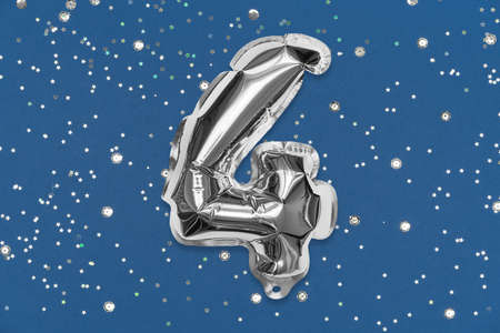 Silver foil balloon number, digit four on a blue background with sequins. Birthday greeting card with inscription 4. Top view. Numerical digit. Celebration event, template.の写真素材