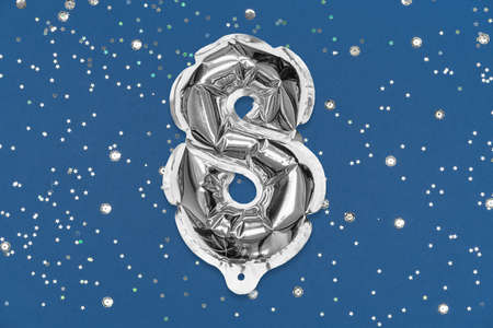 Silver foil balloon number, digit eight on a blue background with sequins. Birthday greeting card with inscription 8. Top view. Numerical digit. Celebration event, template.の写真素材