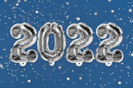 Silver foil balloon number, digit 2022 on a blue background with sequins. New Years card. Happy new...