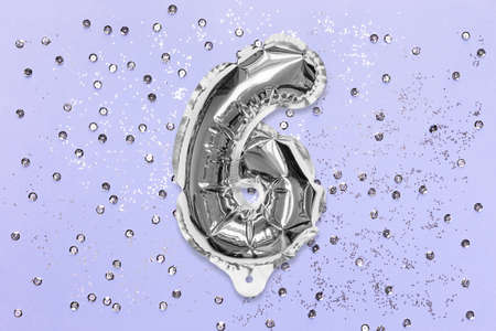 Silver foil balloon number, digit six on a lilac background with sequins. Birthday greeting card with inscription 6. Top view. Numerical digit. Celebration event, template.の写真素材