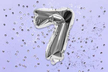 Silver foil balloon number, digit seven on a lilac background with sequins. Birthday greeting card with inscription 7. Top view. Numerical digit. Celebration event, template.の写真素材