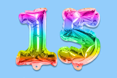 Rainbow foil balloon number, digit fifteen on a blue background. Birthday greeting card with inscription 15. Anniversary concept. top view. Numerical digit. Celebration event template.の写真素材