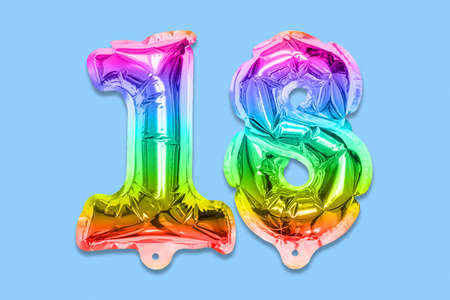 Rainbow foil balloon number, digit eighteen on a blue background. Birthday greeting card with inscription 18. Anniversary concept. top view. Numerical digit. Celebration event template.の写真素材