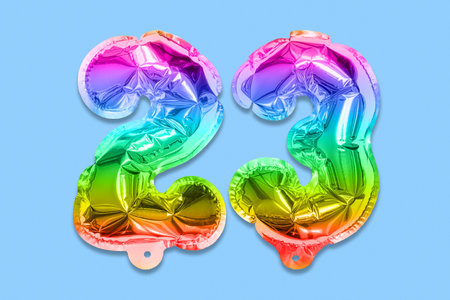 Rainbow foil balloon number, digit twenty three on a blue background. Birthday greeting card with inscription 23. Top view. Numerical digit. Celebration event template.の写真素材