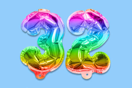 Rainbow foil balloon number, digit thirty two on a blue background. Birthday greeting card with inscription 32. Top view. Numerical digit. Celebration event template.の写真素材