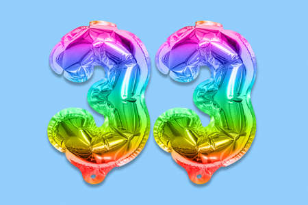 Rainbow foil balloon number, digit thirty three on a blue background. Birthday greeting card with inscription 33. Top view. Numerical digit. Celebration event template.の写真素材
