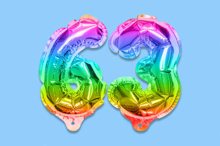 Rainbow foil balloon number, digit sixty three on a blue background. Birthday greeting card with inscription 63. Top view. Numerical digit. Celebration event template.の写真素材