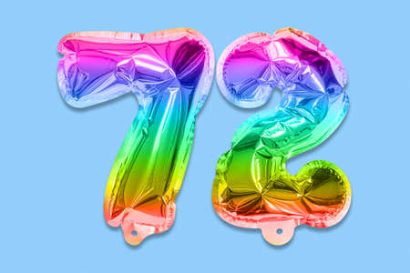 Rainbow foil balloon number, digit seventy two on a blue background. Birthday greeting card with inscription 72. Top view. Numerical digit. Celebration event template.の写真素材