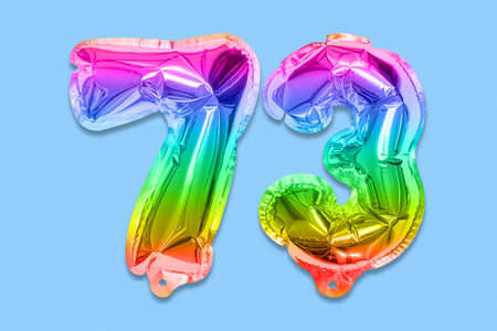 Rainbow foil balloon number, digit seventy three on a blue background. Birthday greeting card with inscription 73. Top view. Numerical digit. Celebration event template.の写真素材