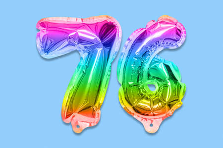 Rainbow foil balloon number, digit seventy six on a blue background. Birthday greeting card with inscription 76. Top view. Numerical digit. Celebration event template.の写真素材