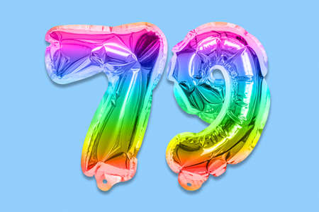 Rainbow foil balloon number, digit seventy nine on a blue background. Birthday greeting card with inscription 79. Top view. Numerical digit. Celebration event template.の写真素材