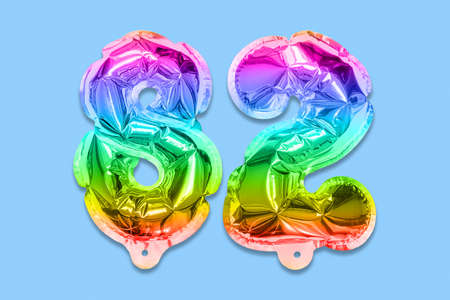 Rainbow foil balloon number, digit eighty two on a blue background. Birthday greeting card with inscription 82. Top view. Numerical digit. Celebration event template.の写真素材