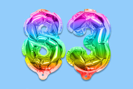Rainbow foil balloon number, digit eighty three on a blue background. Birthday greeting card with inscription 83. Top view. Numerical digit. Celebration event template.の写真素材