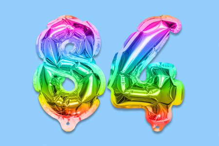 Rainbow foil balloon number, digit eighty four on a blue background. Birthday greeting card with inscription 84. Top view. Numerical digit. Celebration event template.の写真素材