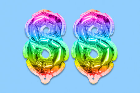 Rainbow foil balloon number, digit eighty eight on a blue background. Birthday greeting card with inscription 88. Top view. Numerical digit. Celebration event template.の写真素材