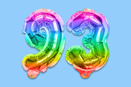 Rainbow foil balloon number, digit ninety three on a blue background. Birthday greeting card with inscription 93. Top view. Numerical digit. Celebration event template.の写真素材