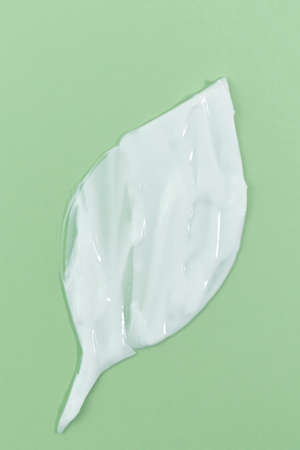 White creamy texture in the shape of a leaf on a green background. Smear of skincare cosmetics product. wellness and beauty conceptの写真素材